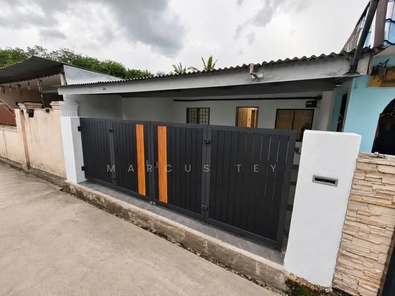 Exterior features: black wooden gate with wooden accents, concrete wall, grey concrete driveway, single-storey building, roof with overhang, exterior wall painted in light colour, windows with wooden frames, surrounding greenery; style: modern.