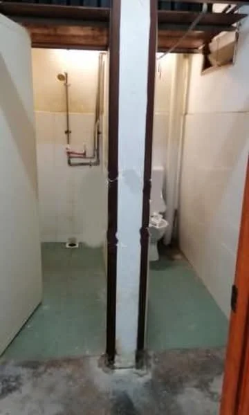 Room features: tile flooring, white tiled walls, toilet, shower head, plumbing fixtures, partition wall, green vinyl flooring, exposed ceiling beams.