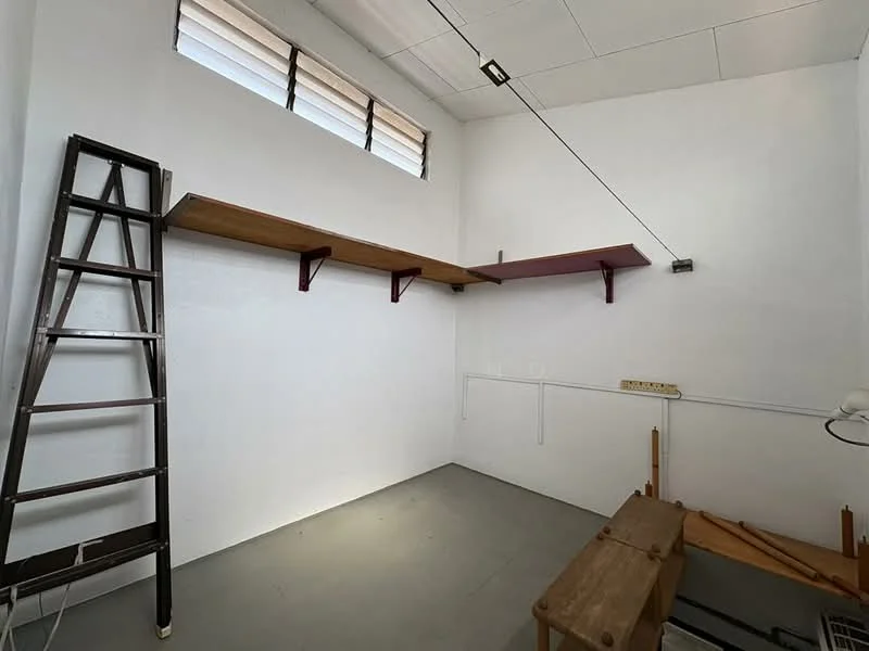 Room features: white painted walls, grey concrete flooring, wooden shelves mounted on wall, metal ladder, wooden workbench, overhead lighting, exposed electrical wiring, window with horizontal slats; style: minimalist.