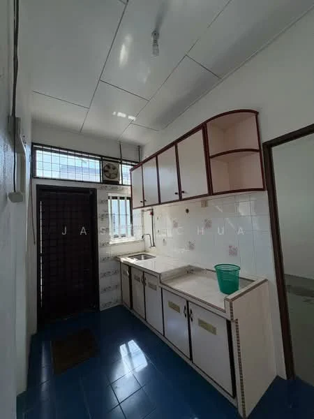 Kitchen features: white cabinetry with red accents, single-bowl sink, countertop with backsplash, blue ceramic tile flooring, window with grid pattern, door leading to exterior, wall-mounted light fixture, open shelving, green plastic bucket.