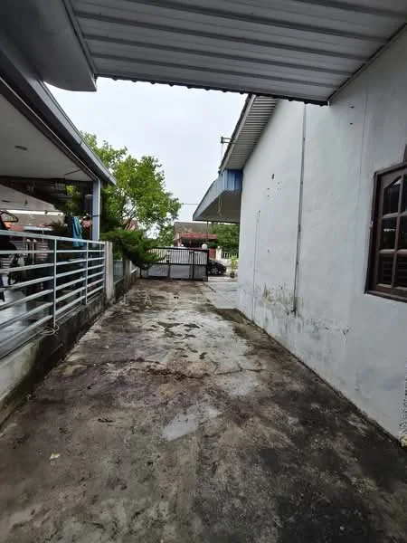 Exterior features: concrete flooring, white painted walls, metal roof, fenced entrance gate, surrounded by greenery, driveway, overhang from roof.