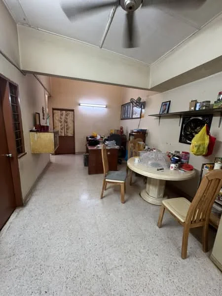 Room features: light-colored walls, ceiling with exposed beams, ceiling fan, table with round top, two wooden chairs, wooden desk, shelves on wall, various items on shelves, door leading to another room, window with grille, tile flooring.