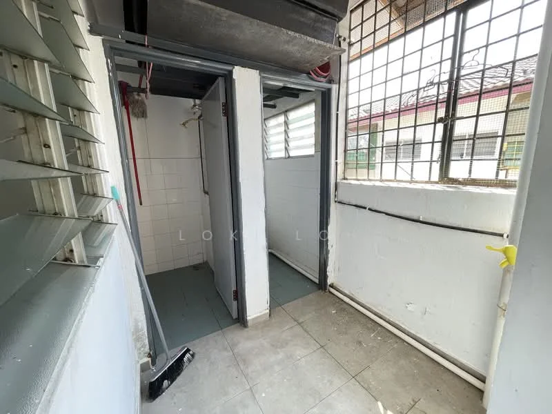 Room features: white painted walls, grey tiled flooring, window with metal grilles, shower area with tiled walls, exposed plumbing, light fixture on ceiling, doorway leading to another room, corner space with natural light.