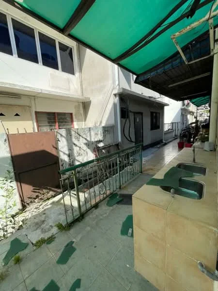 Exterior type: linked terrace house; features: green awning, tiled flooring, exposed concrete walls, metal railing, outdoor sink with two basins, narrow walkway, adjacent buildings, outdoor space with plants; style: modern.