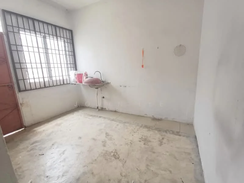 Room features: white painted walls, concrete flooring, single window with metal bars, red metal door, sink with no visible faucet, wall-mounted shelf, no visible lighting fixtures.