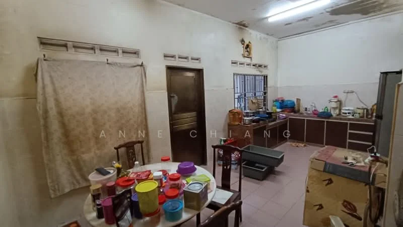 Kitchen features: white painted walls, tile flooring, wooden cabinets, stainless-steel sink, countertop with storage, window with metal grille, table with assorted containers, kitchen appliances visible, refrigerator, cooking utensils, shelves with dishes.