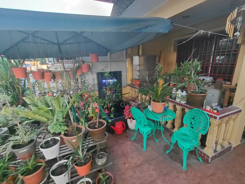 Room features: green outdoor chairs, small round table, various potted plants, decorative plant stand, awning for shade, tile flooring, garden hose, watering can, wall-mounted decorations, fenced area; style: tropical; view: garden.