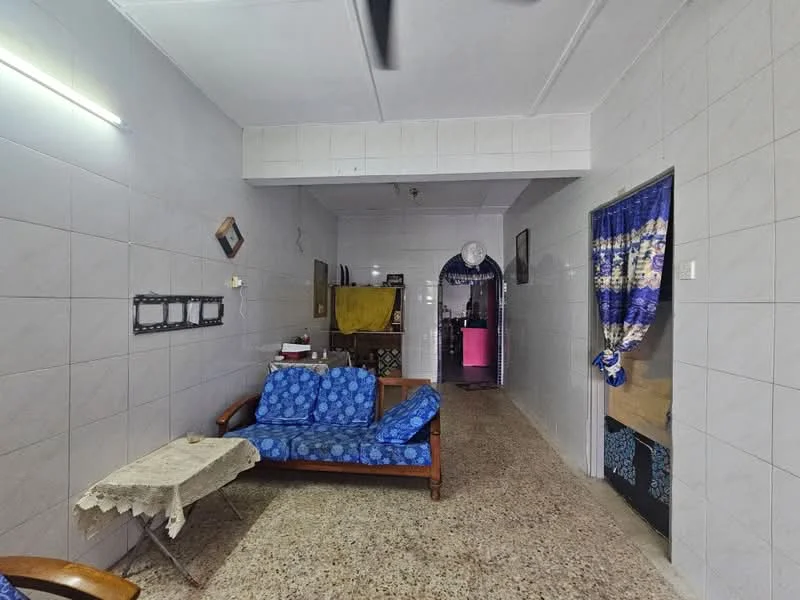 Living features: blue fabric sofa, wooden frame for sofa, coffee table with lace tablecloth, white tiled walls, grey tiled flooring, ceiling light fixture, decorative wall art, curtains with blue and gold pattern, arched doorway leading to kitchen, open layout to adjacent room.