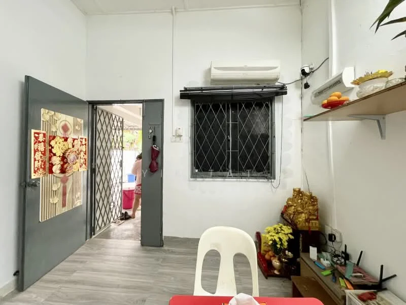 Room features: white painted walls, grey laminate flooring, window with black grille, wall-mounted air conditioning unit, open shelving, decorative items on shelf, door with decorative panel, light switch, power outlet.