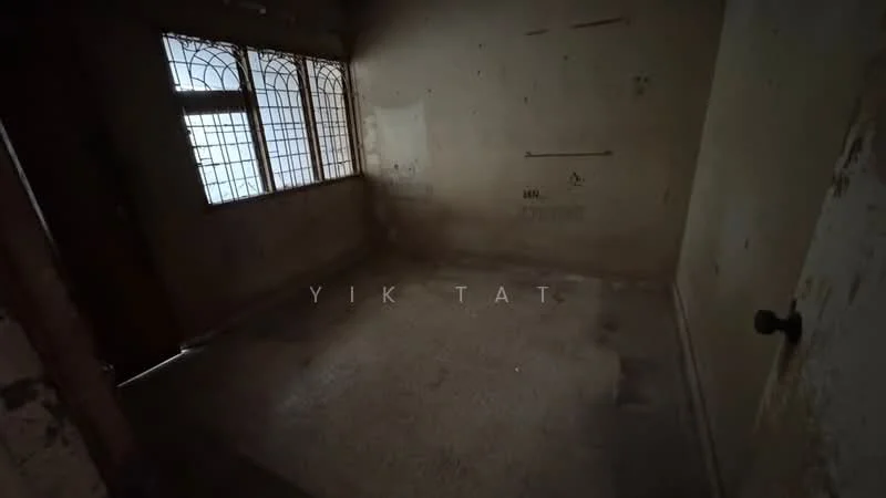 Room features: bare concrete flooring, unpainted walls with peeling paint, two windows with decorative metal grilles, single door, no visible fixtures or furnishings.