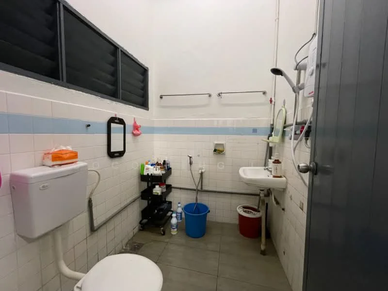 Bathroom features: white tiled walls, grey floor tiles, toilet, sink with faucet, mirror, wall-mounted soap dispenser, towel rack, bucket, storage cart, water heater, window with black grilles.