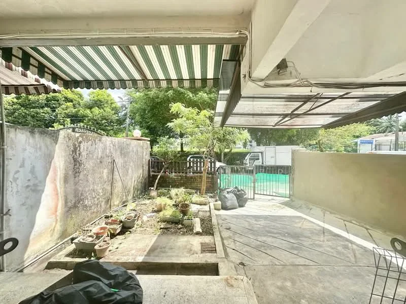 Exterior features: paved flooring, garden area with potted plants, fenced perimeter, awning for shade, greenery visible in background, concrete wall, outdoor space.