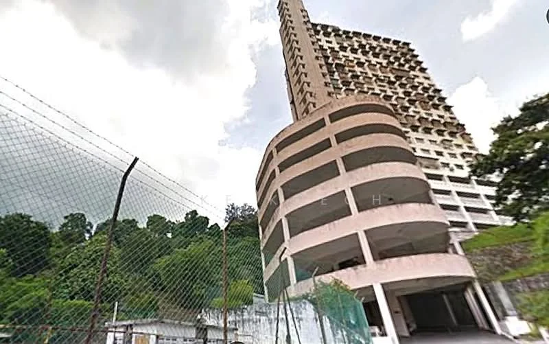Exterior type: high-rise condominium; features: concrete facade, balconies on upper floors, multi-storey structure, surrounded by greenery, fenced perimeter, parking area visible, elevated position, cloudy sky in background; style: modern.