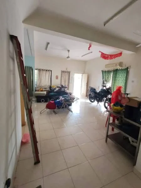 Living features: white painted walls, ceramic tile flooring, ceiling fan, two large windows with sheer curtains, door leading to outdoor area, decorative red banners, multiple pieces of furniture including a sofa and chairs, motorcycles parked inside, ladder against the wall, storage shelves, various household items scattered.