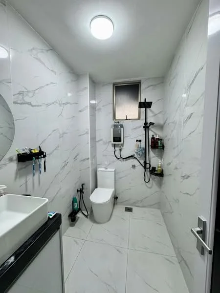 Bathroom features: white one-piece toilet, walk-in shower with handheld shower head, chrome shower mixer, black countertop with sink, round mirror, white marble tile walls, grey marble tile flooring, wall-mounted storage shelves, window for natural light, recessed ceiling light; style: modern.