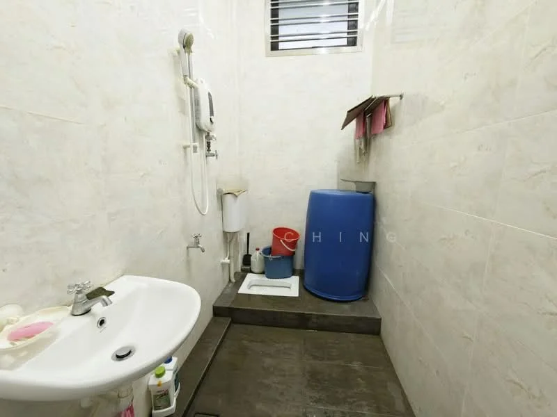 Bathroom features: white ceramic sink, chrome basin mixer faucet, shower head, wall-mounted shower fixture, white tiled walls, grey tile flooring, blue plastic barrel, toilet, toilet paper holder, small window for ventilation.