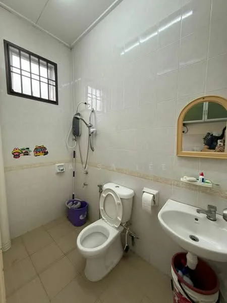 Bathroom features: white tiled walls, cream tiled flooring, one-piece toilet, sink with mirror, shower with handheld showerhead, toilet paper holder, wall-mounted soap dispenser, small window for ventilation, decorative wall stickers, plunger in purple bucket.