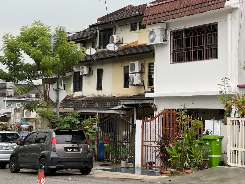 Exterior type: linked terrace house; features: two-storey building, white painted facade, brown tiled roof, multiple wall-mounted split AC units, front gate with metal bars, driveway with interlocking pavers, manicured landscaping with small trees, visible parking area, green waste bin, surrounded by residential neighborhood; style: modern.