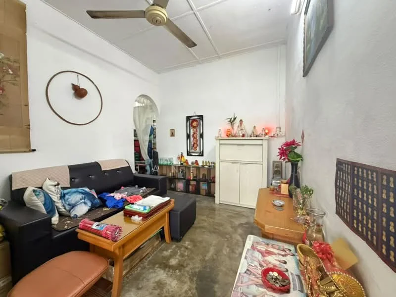 Living features: black leather sofa, wooden coffee table, decorative wall art, white painted walls, exposed concrete flooring, ceiling fan, shelves with decorative items, small altar with offerings, table with colorful textiles, wall-mounted mirror; style: traditional.