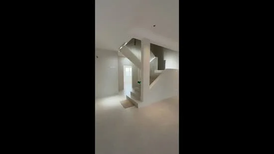 Room features: white painted walls, light-colored flooring, staircase with concrete steps, handrail, recessed lighting, large window for natural light, open space layout, neutral color palette; style: modern.