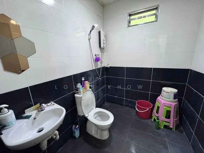 Bathroom features: white tiled walls, black tiled walls, ceramic tile flooring, one-piece toilet, wall-mounted shower, shower head, sink with pedestal, mirror with hexagonal design, plastic stool, waste bin, cleaning supplies, shower curtain rod.