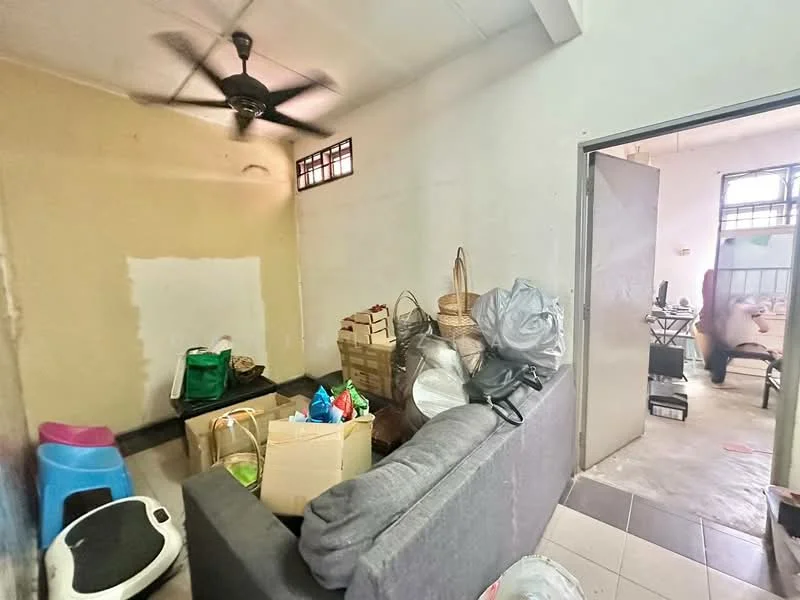 Room features: grey fabric sofa, ceiling fan, white painted walls, black tiled flooring, boxes and bags of items, open doorway to another room, small window with metal grille, scattered household items.