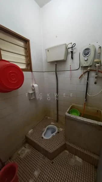 Bathroom features: squat toilet, wall-mounted water tank, shower area, sink with tap, tiled flooring, white tiled walls, window for ventilation, bucket and cleaning supplies.