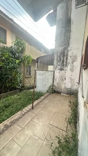 Exterior features: fenced yard, paved walkway, overgrown grass, exposed concrete wall, adjacent residential buildings, partially shaded area, utility lines overhead.
