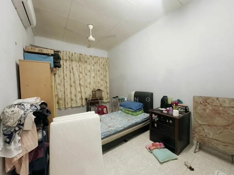 Bedroom features: single bed with mattress, wooden bedside table, ceiling fan, curtains with floral pattern, light-colored walls, tile flooring, clothes on the floor, folding chair, dressing table with mirror, storage cabinet.