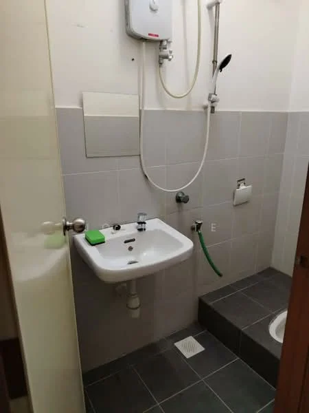 Bathroom features: white wall tiles, grey floor tiles, single-bowl sink, chrome basin mixer faucet, shower head with wall-mounted holder, toilet roll holder, exposed plumbing, drain in floor, water heater unit, green cleaning product on sink.