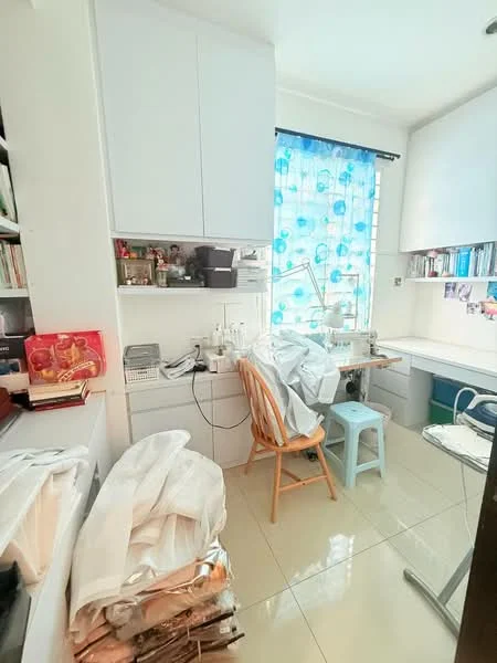 Room features: white cabinetry, blue patterned curtains, white tiled flooring, desk with chair, sewing machine, various storage boxes, piles of fabric, bookshelves with books, table lamp; style: modern.