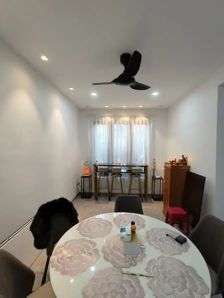 Dining features: round dining table with floral design, 4 upholstered dining chairs, 5-blade ceiling fan with light, white painted walls, tile flooring, large window with sheer curtains, decorative wall shelf, small red stool, decorative items on the table; style: modern.