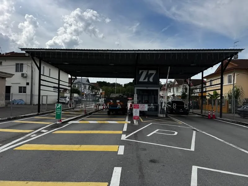 Exterior type: main entrance gate; features: covered entrance structure, security booth, traffic control barriers, marked parking spaces, road markings, surveillance cameras, fenced perimeter, signage for entry, paved driveway, landscaping with trees; style: modern.