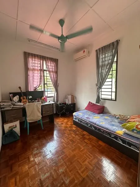 Bedroom features: parquet wood flooring, white painted walls, ceiling fan, two windows with grilles, desk with chair, guitar on desk, bed with colorful bedding, decorative pillows, air conditioning unit, curtains, storage boxes.