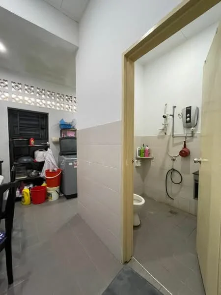 Room features: grey tiled flooring, white painted walls, toilet, shower with wall-mounted showerhead, water heater, sink, storage shelves, black plastic chair, refrigerator, various cleaning supplies in containers.