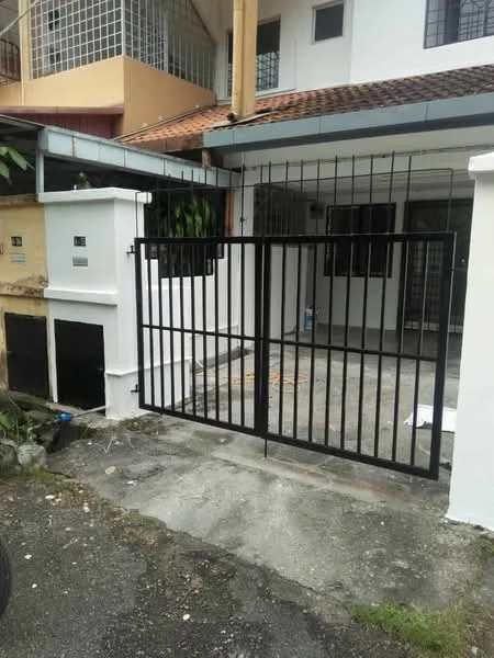 Exterior type: linked terrace house; features: black metal gate, paved driveway, white painted facade, grilled windows, front porch area, surrounding greenery, single-storey structure, roof overhang; style: modern.