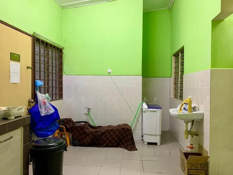 Laundry features: green painted walls, white tiled walls, grey tiled flooring, washing machine, sink with faucet, plastic chair, black trash bin, hose, brown blanket, window with metal bars.
