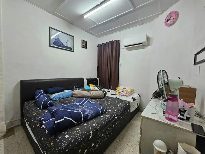 Bedroom features: two beds with dark upholstered headboards, bedding with star pattern, white walls, ceiling with fluorescent lighting, wall-mounted air conditioning unit, brown curtains, framed artwork on wall, fan on bedside table, wooden bedside table, pink water bottle, decorative items on table.