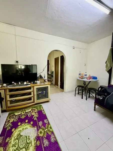 Living features: white painted walls, tile flooring, ceiling lights, large flat-screen TV, wooden TV console, decorative items on console, purple area rug with floral pattern, dining table with black legs, plastic dining chairs, arched doorway leading to another room, doorway to hallway, window with curtain, black duffel bag.