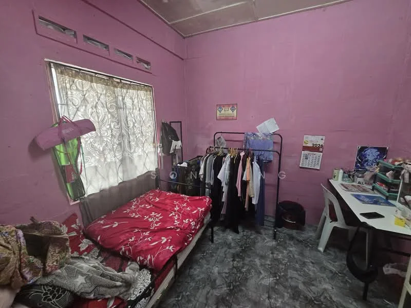 Bedroom features: pink painted walls, vinyl flooring, single bed with red floral bedding, clothing rack with hanging clothes, window with sheer curtains, desk with chair, calendar on wall, decorative wall art.