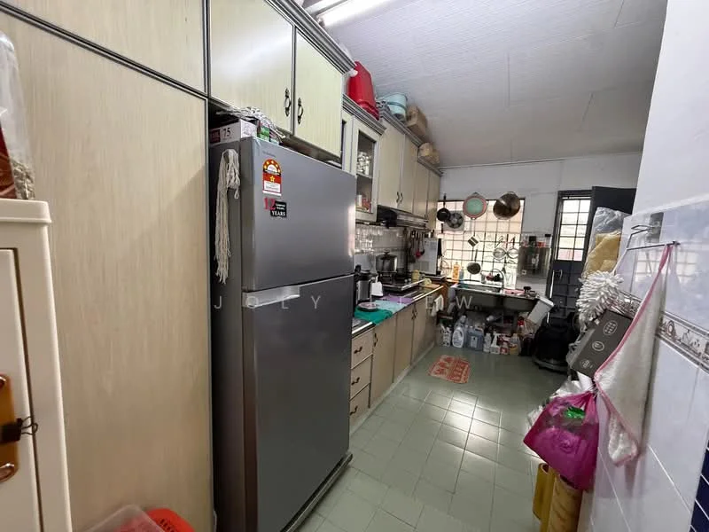 Kitchen features: stainless-steel fridge, wood cabinetry with cream finish, green tile flooring, white tiled backsplash, double-basin sink, chrome faucet, wall-mounted shelves, countertop with appliances, window with metal grille, hanging pots and pans, various kitchen utensils, plastic storage containers.