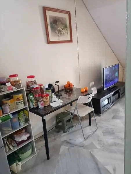 Living features: marble flooring, white painted walls, angled ceiling, wall-mounted TV, wooden TV console, small dining table, plastic folding chair, various food containers on shelves, fruit bowl with oranges, table lamp, green stool.