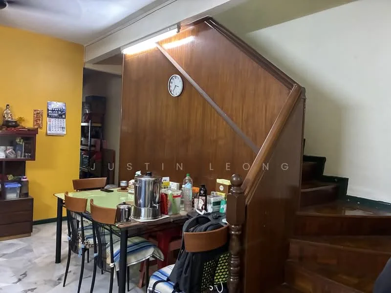 Dining features: wooden dining table, black dining chairs, wooden staircase, clock on wall, yellow painted wall, marble flooring, shelves with decorative items, various kitchen items on table.