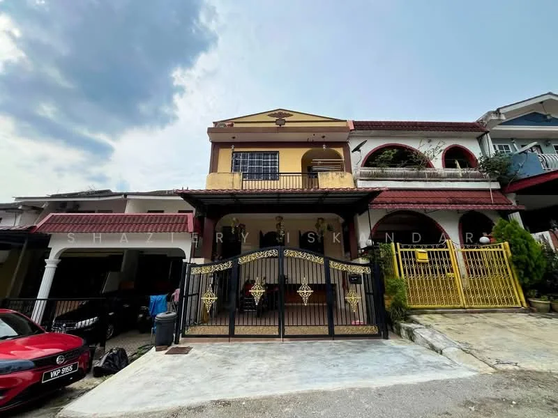 Exterior type: linked terrace house; features: two-storey building, yellow painted facade, red tiled roof, black wrought iron gate, front porch with car parking, balcony on the upper floor, decorative wall features, manicured shrubs, paved driveway, surrounded by other residential buildings; style: modern.