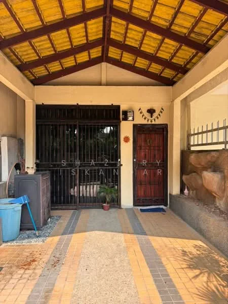 Exterior features: yellow painted ceiling with wooden beams, tiled flooring in beige and grey pattern, black metal security gate, wooden front door with decorative elements, small potted plant near the entrance, concrete wall with decorative stone cladding, open porch area, blue plastic trash bin, visible sunlight casting shadows; style: traditional.