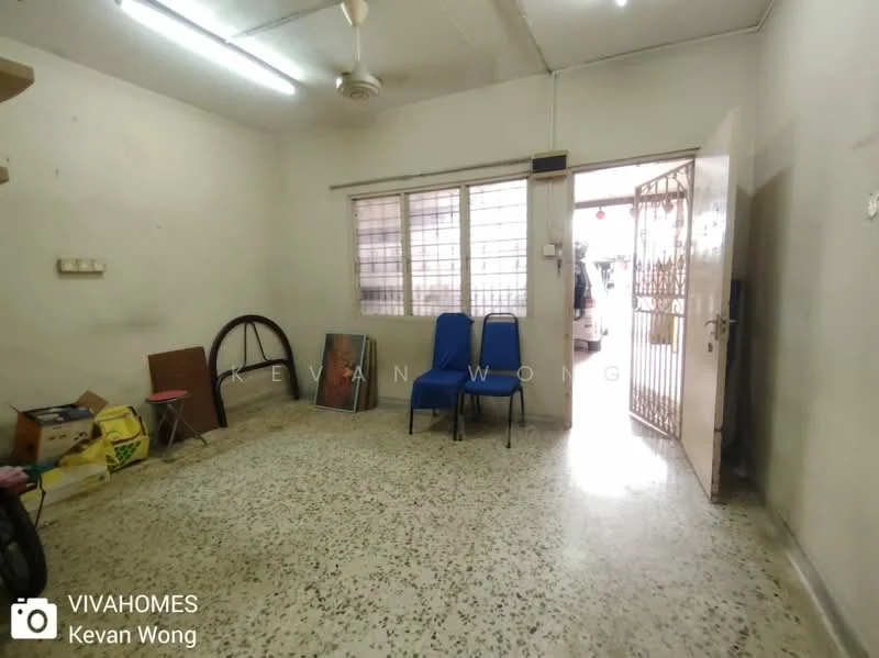 Room features: exposed concrete flooring, white painted walls, ceiling fan, large window with metal grille, wooden door, two blue chairs, metal frame for a chair, storage boxes, light fixtures on ceiling; style: minimalist.