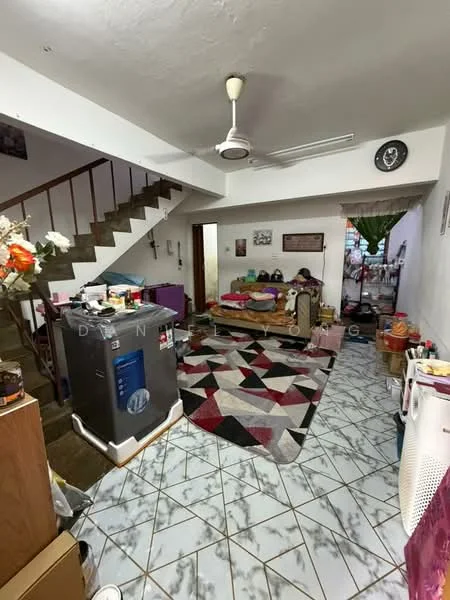 Living features: 5-blade ceiling fan with light, area rug with geometric pattern, sofa in beige, coffee table, wall-mounted clock, staircase leading to upper floor, decorative plants, wall-mounted artwork, tile flooring with diamond pattern, open layout to adjacent room. Room features: washing machine, wooden staircase, decorative items on shelves, doorway leading to another room.