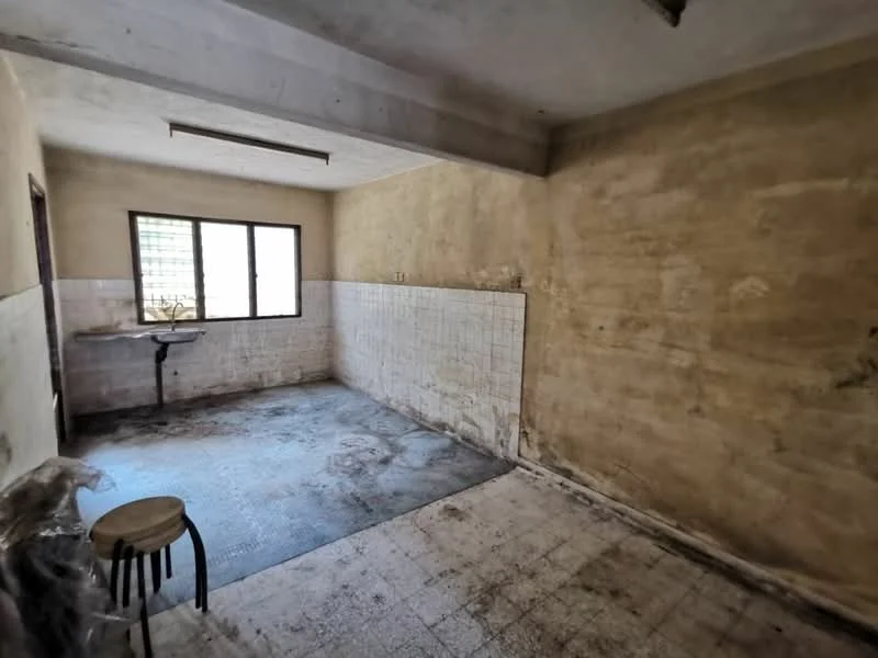 Room features: bare concrete walls, unpainted walls, tile cladding on lower half of walls, dirty floor tiles, single small window, exposed ceiling beams, stool, sink with no visible faucet, no visible cabinetry, no visible appliances.