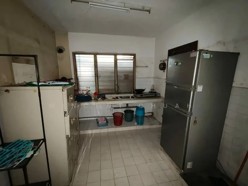 Kitchen features: white tiled walls, grey tiled flooring, single-bowl stainless-steel sink, chrome faucet, built-in countertop, double-door fridge, cabinets with handles, window with horizontal slats, plastic buckets in various colors, wall-mounted light fixture, open shelving.