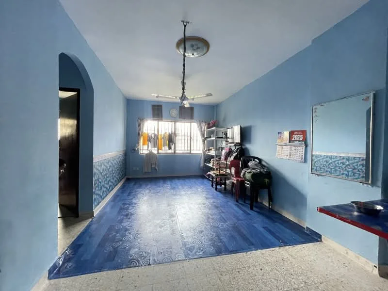 Room features: blue painted walls, ceiling fan, window with curtains, tile flooring, mirror on wall, wooden shelving unit, calendar on wall, two chairs, table with red surface, decorative wall border.